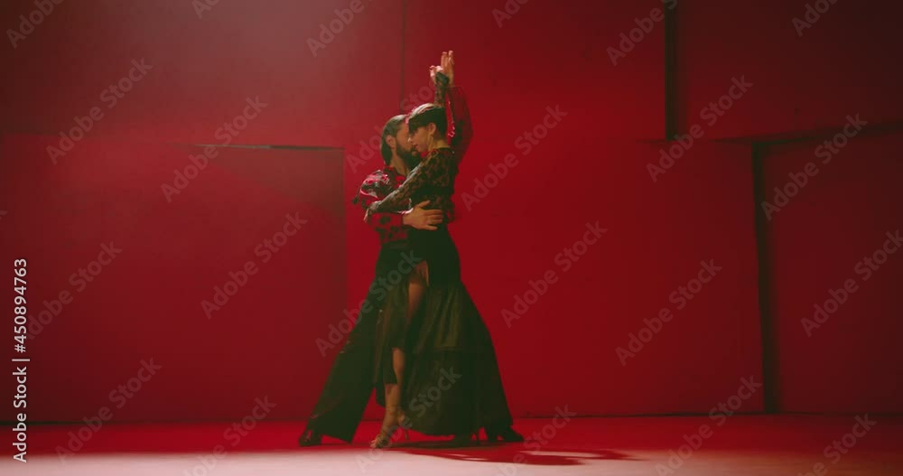 4K Beautiful couple dancing latin dance . Professional dancers dancing flamenco, rumba or salsa on red background. Pair in spanish dress performs dance movement. Shot ARRI ALEXA Camera in Slow Motion