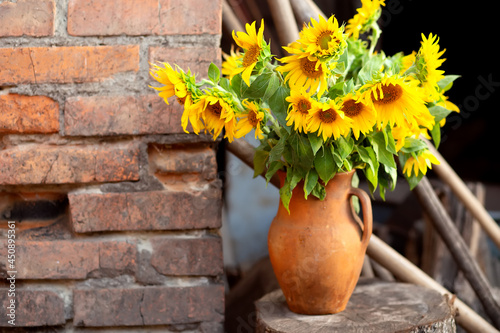 Bouquet of blooming sunflowers in old clay jug near red brick wall background, selective focus