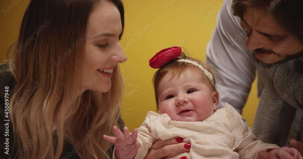 Portrait of happy family . Mother and father playing, hugging and kissing infant daughter . Sweet baby girl with parents on yellow background. Studio shot on RED Epic Cinema Camera in slow motion Portrait of happy family . Mother and father playing, hugging and kissing infant daughter . Sweet baby girl with parents on yellow background. Studio shot on RED Epic Cinema Camera in slow motion