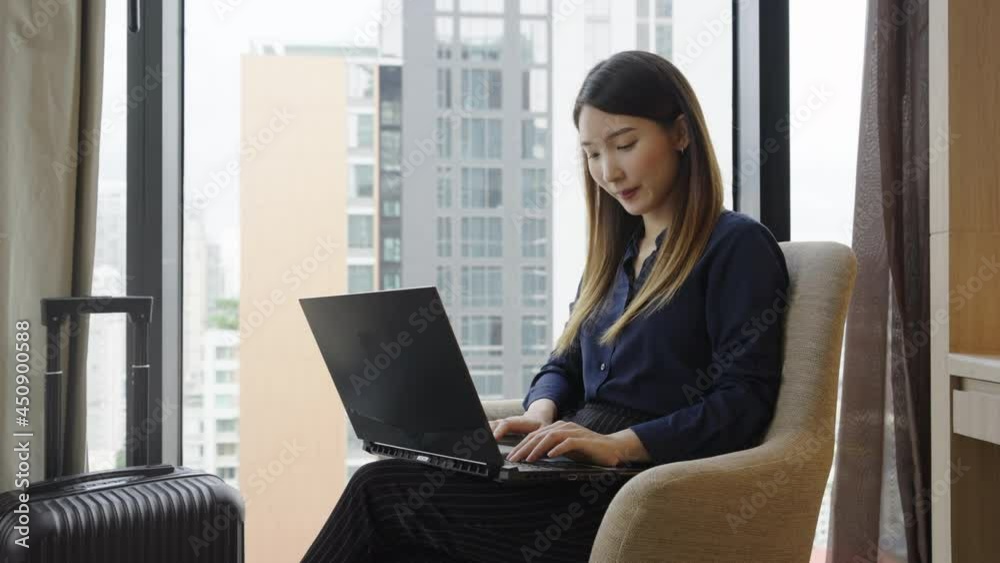 Asian businesswoman using laptop working in hotel room remotely on her business travel Asian businesswoman using laptop working in hotel room remotely on her business travel