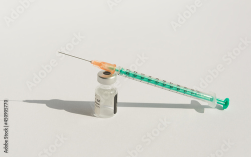 Close-up dose vaccine vial and injection syringe on a white background. The bottle and syringe cast a harsh shadow. Coronavirus vaccination concept.