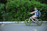 Side full length portrait of school child on a bicycle at asphalt road in early morning. Boy on bike in the city