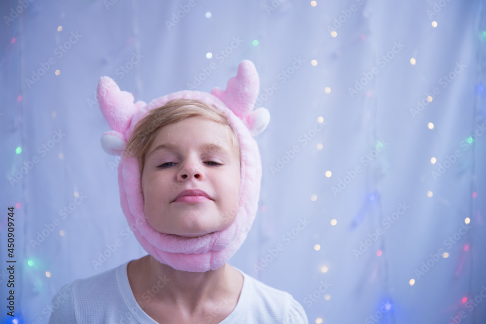 The child is fooling around. A girl posing in a New Year's hat in the form of deer horns. Preparing for the new year and christmas. Portrait of a beautiful child expecting a holiday The child is fooling around. A girl posing in a New Year's hat in the form of deer horns. Preparing for the new year and christmas. Portrait of a beautiful child expecting a holiday