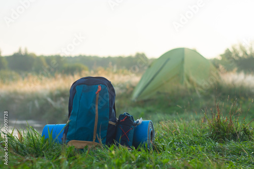Sports backpack with a rug near a tourist tent on the background of nature and forest.