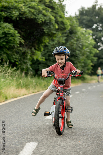 Child riding bicycle on the bike path at rain. Kid in helmet learning to ride at summer. Happy boy riding bike, having fun outdoors on nature.