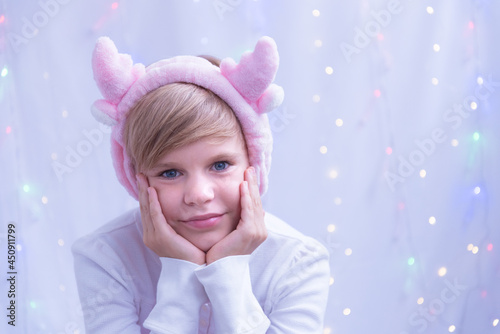 Portrait of a very beautiful child with blond hair. Girl with Christmas reindeer horns. A light smile and an attentive look. Bright blue eyes. The child is preparing for the New Year and Christmas