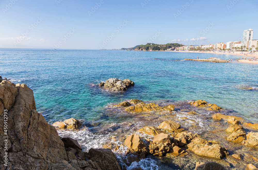 Rocky coast and sandy beach of the small Spanish resort of Lloret de Mar on a sunny summer day.