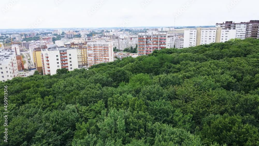 Aerial flight over large overgrown green wild forest overlooking city buildings Aerial flight over large overgrown green wild forest overlooking city buildings