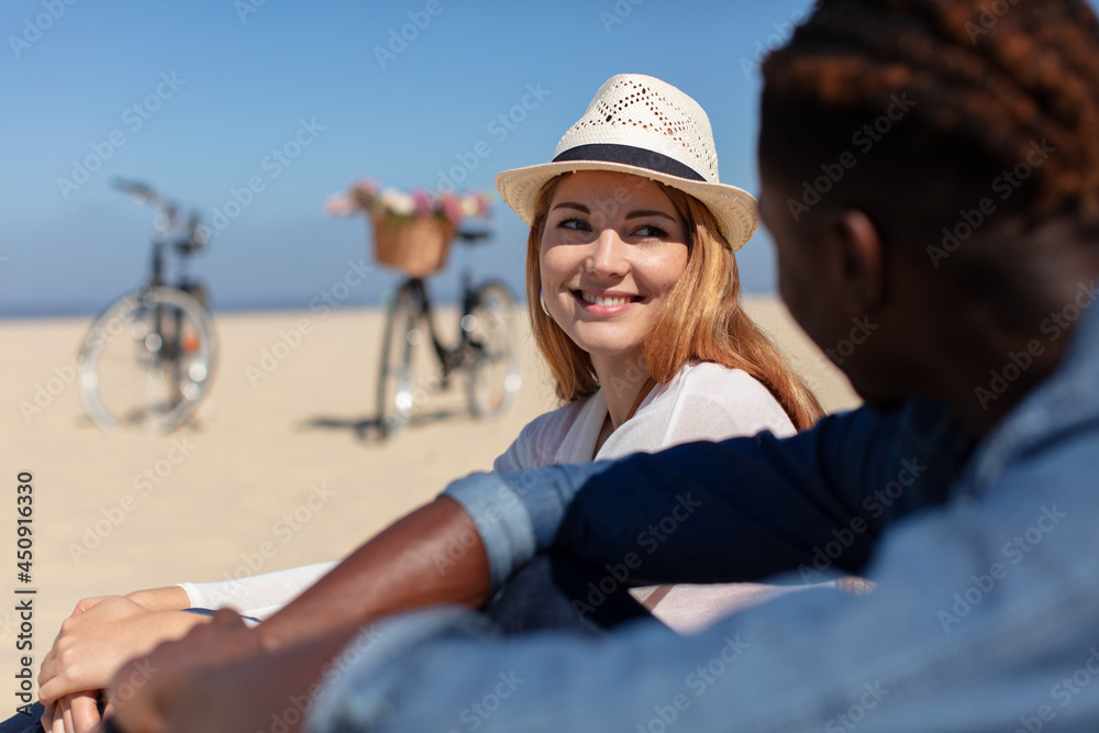 happy young couple sitting on beach with bicycles on background