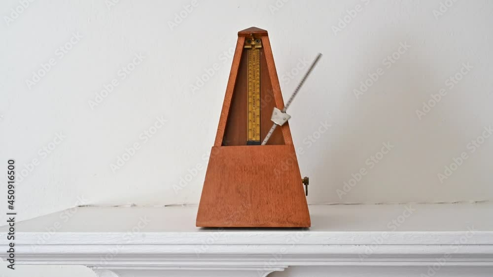An old fashioned metronome beating at an Andante pace on a white shelf.