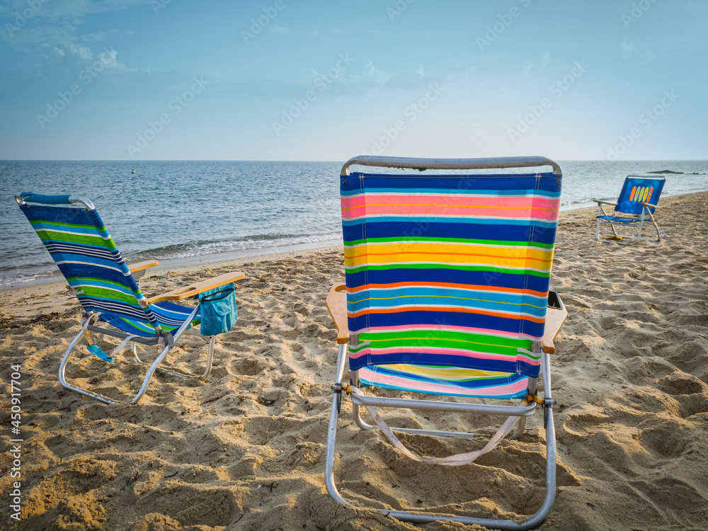 Vibrant striped beach chairs on the beach. Three empty chairs waiting for vacationers to arrive. Vibrant striped beach chairs on the beach. Three empty chairs waiting for vacationers to arrive.