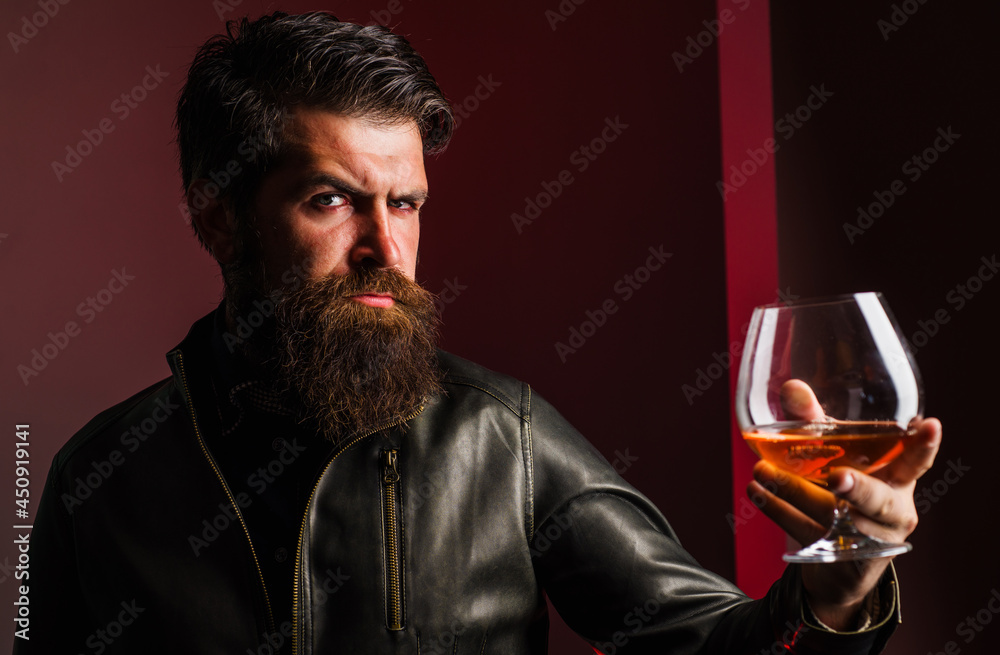 Expensive drink. Male in leather jacket drinking brandy or cognac. Bearded man with glass of whiskey. Expensive drink. Male in leather jacket drinking brandy or cognac. Bearded man with glass of whiskey.