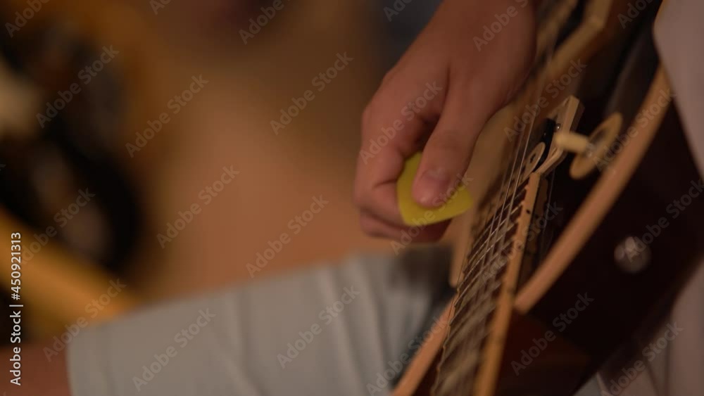 Mano de musico tocando guitarra electrica con una pua grande amarilla