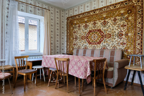 Example of Old Soviet Russian poor interior in Khruschev House. Aged  sideboard, table, chairs, sofa. Shabby floor. Tattered wallpaper on the wall. Paper butterflies as decor. Apartment of pensioners.