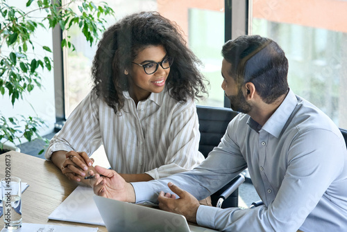 Happy young female African American businesswoman with clasped hands listening to indian executive manager ceo. Diverse multiracial professional group discussing business plan at board room meeting.