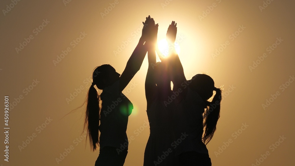 Silhouette of group of people greet each other with their hands at sunset. Teamwork, business group. Active women rejoice in success and victory. Girls in rays of sun greet in park in rays of sun.