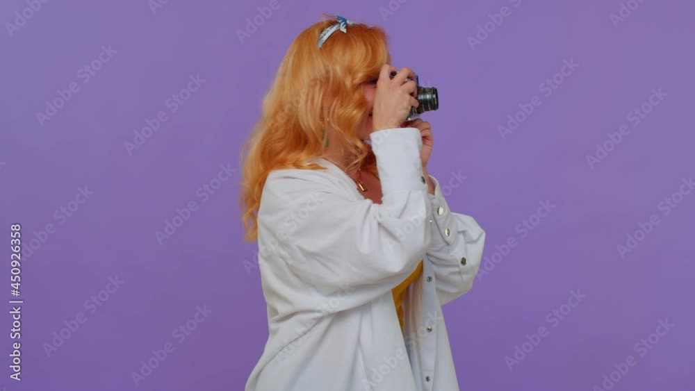 Red hair stylish girl tourist in white shirt. Photographer taking photos on retro camera and smiling. Young woman on purple studio background. People sincere emotions. Travel, summer holiday vacation Red hair stylish girl tourist in white shirt. Photographer taking photos on retro camera and smiling. Young woman on purple studio background. People sincere emotions. Travel, summer holiday vacation