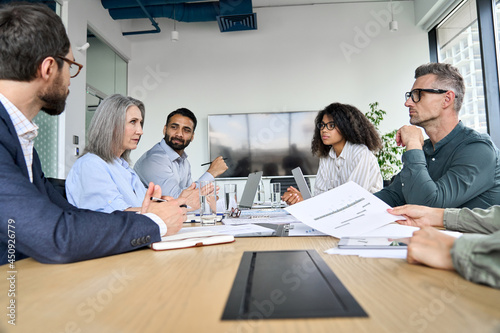 Photo Diverse professional executive business team people discuss project sitting at meeting table in board room