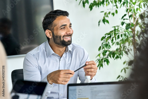 Canvas Print Friendly happy smiling ceo Indian businessman holding pen in hand looking listening to colleague discussing global corporation research report at table
