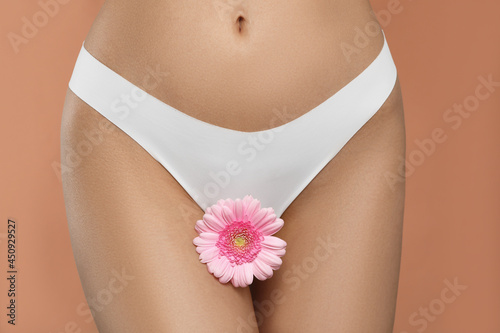 Woman in white panties with gerbera flower on peach background, closeup