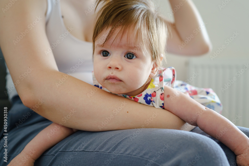 Small caucasian baby girl in the lap of her mother while sitting on the sofa at home - motherhood and parenting concept real people growing up in bright summer day Small caucasian baby girl in the lap of her mother while sitting on the sofa at home - motherhood and parenting concept real people growing up in bright summer day