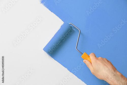 Man applying orange paint with roller brush on white wall, closeup