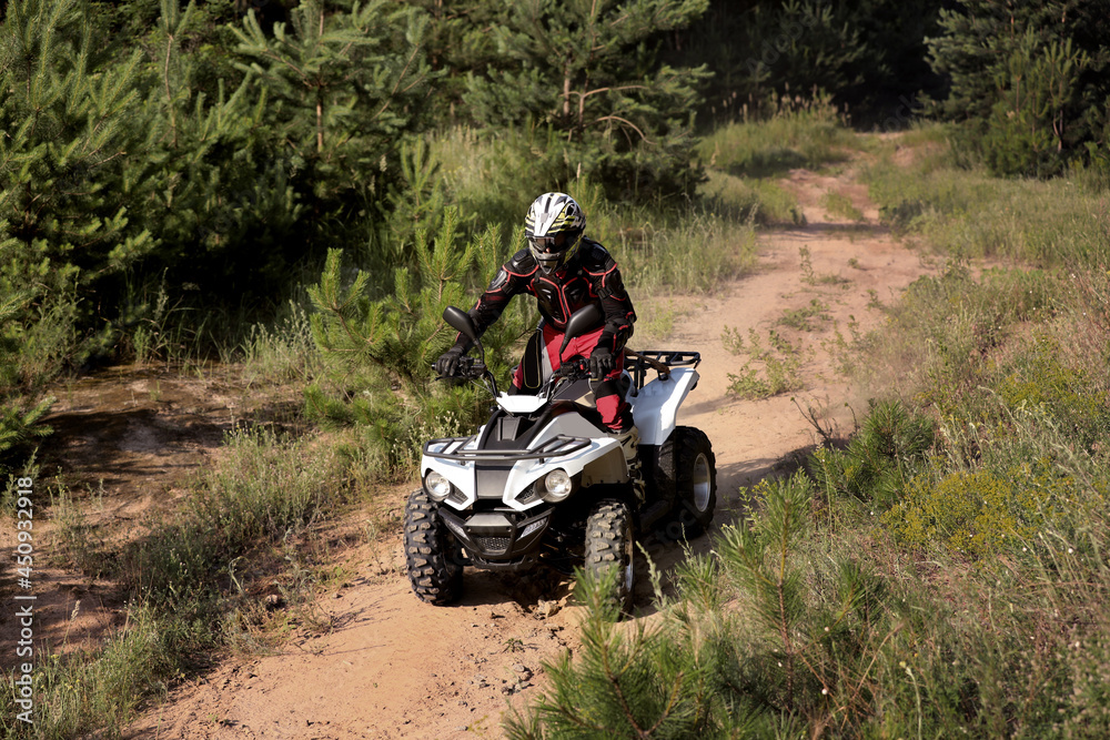 Man driving modern quad bike on sandy road near forest. Extreme sport Man driving modern quad bike on sandy road near forest. Extreme sport