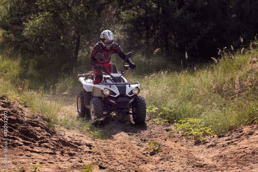 Man driving modern quad bike on sandy road near forest. Extreme sport Man driving modern quad bike on sandy road near forest. Extreme sport