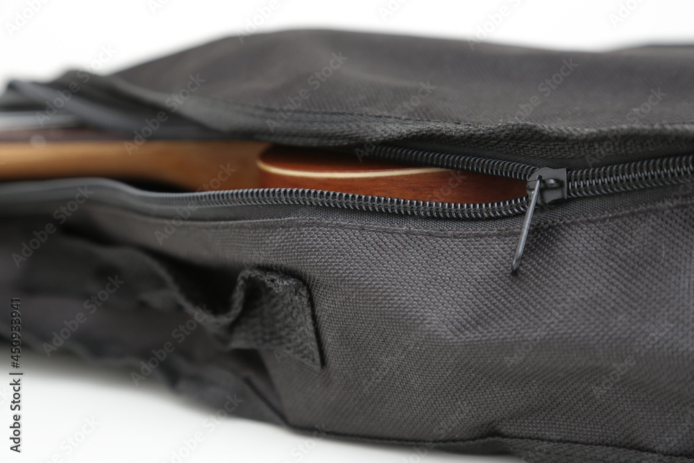 Small brown wooden ukulele guitar in black cover.
Small brown wooden ukulele guitar in black cover.