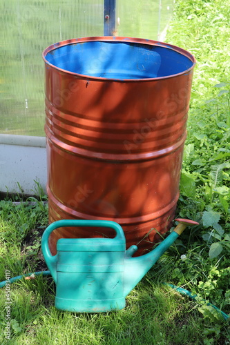 An iron water barrel and a plastic watering can.