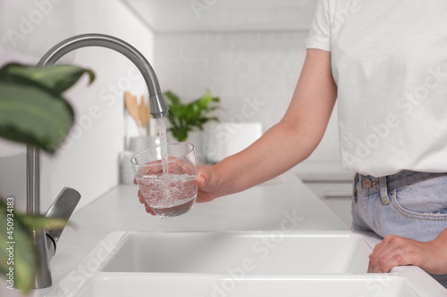Woman filling glass with water from tap in kitchen, closeup photo