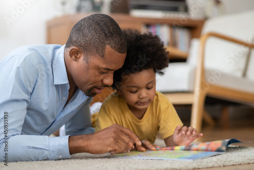 African American Father and his baby boy lying reading book on the floor