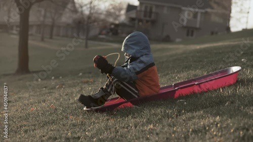 Boy in winter clothes on sledding hill wishes for snow