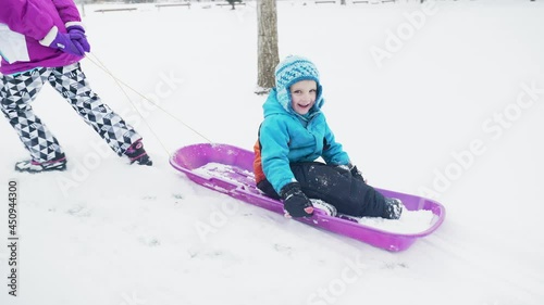 Young girl pulls children in a sled in the snow in the winter