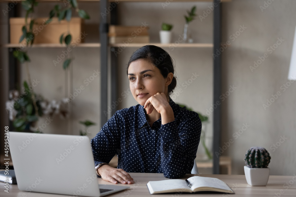 Pensive young Indian woman sit at desk at home office work on laptop look in distance thinking pondering. Thoughtful millennial biracial female distracted from computer job plan or visualize. Pensive young Indian woman sit at desk at home office work on laptop look in distance thinking pondering. Thoughtful millennial biracial female distracted from computer job plan or visualize.