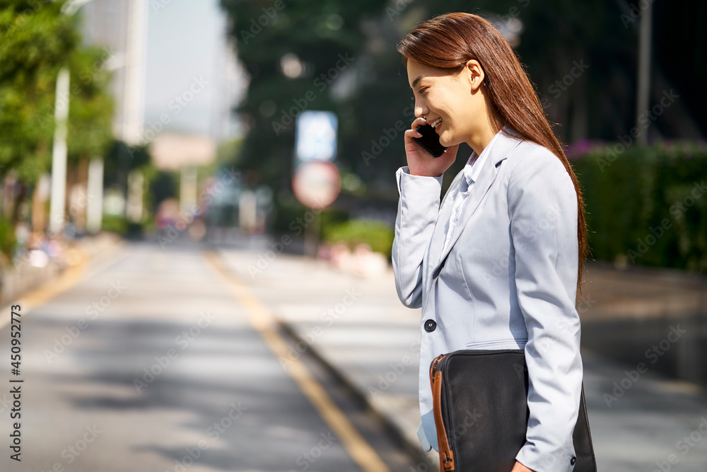 young asian white collar office lady talking on cellphone while walking in street