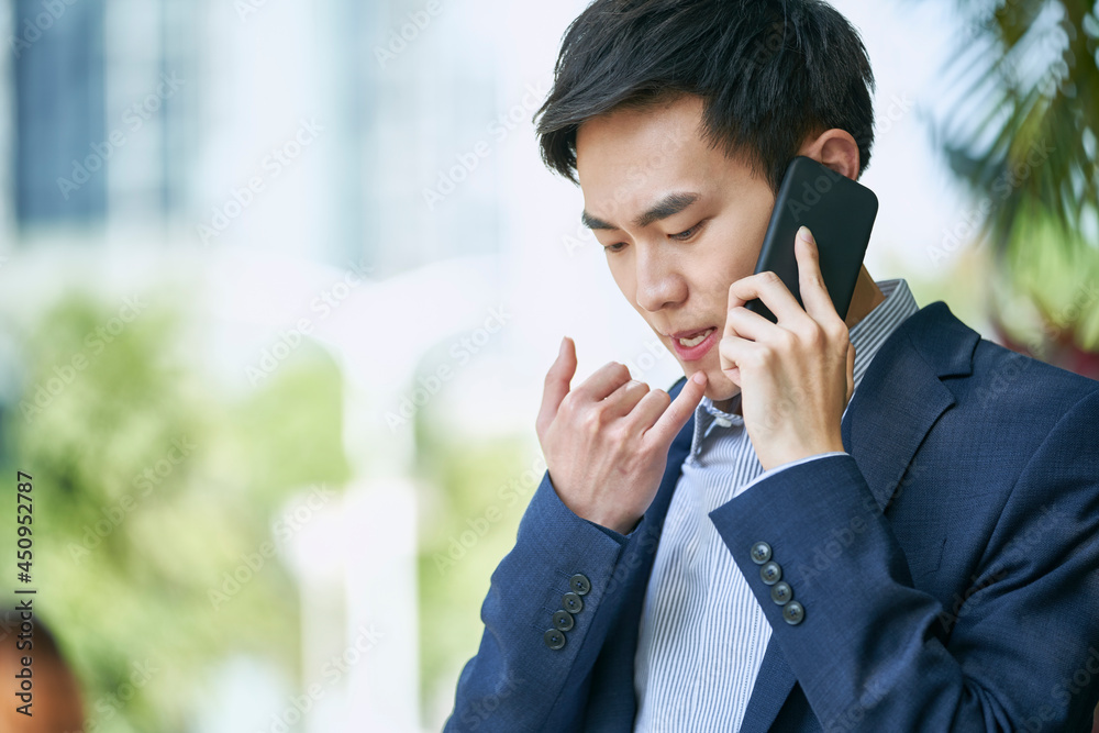 young asian business man talking on cellphone outdoors on city street young asian business man talking on cellphone outdoors on city street