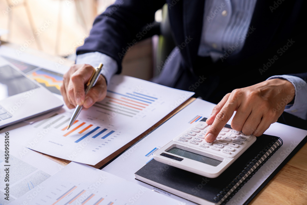 Accountant or banker working process, a Businesswoman using a calculator to calculate the numbers of statistic business profits growth rate on documents graph data, his desk in an office. Accountant or banker working process, a Businesswoman using a calculator to calculate the numbers of statistic business profits growth rate on documents graph data, his desk in an office.