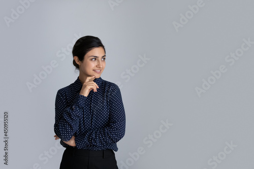 Smiling young Indian woman isolated on grey studio background look at blank empty copyspace aside thinking. Happy biracial female client consider good sale deal or promotion offer. Copy space concept.