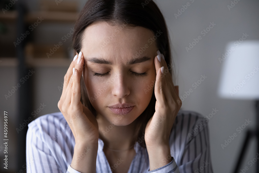 Close up of sick millennial Caucasian woman touch temples struggle with migraine or headache. Unhappy unhealthy young female close eyes suffer from blurry vision or dizziness. Healthcare concept.