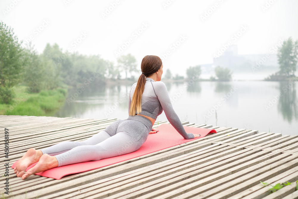 Woman dressed leggings and top with pink mat doing yoga on summer park.Healthy sport lifestyle concept