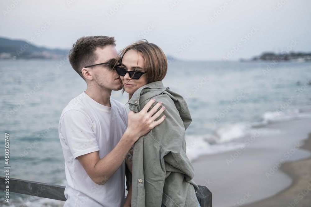Stylish couple cuddle on the beach. Beautiful seaview on the background. wearing sunglasses. High quality photo