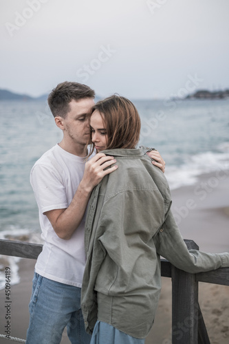 Portrait of romantic Couple standing on the beach. Wearing sunglasses and casual clothes. Boyfriend gave girlfriend his shirt. Millennials. 