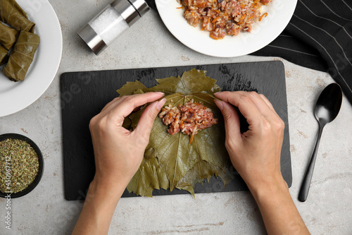 Top view of woman preparing stuffed grape leaves at light table, closeup photo