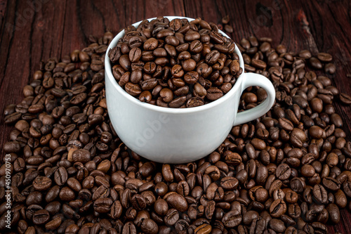 Scattered on the table beans of roasted coffee in a white cup. Morning. Cheerfulness