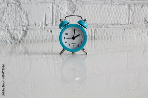 Close-up of blue Table Alarm Clock with bells on white table and white cement wall background. time concept.