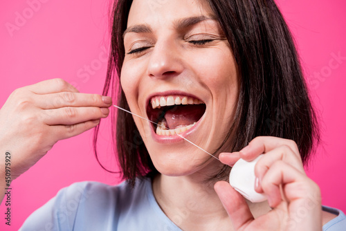 Beautiful young woman use dental floss on pink background