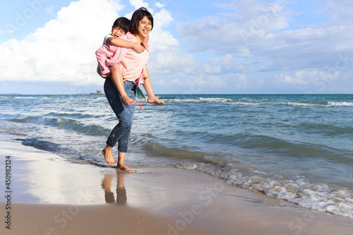 Mother piggybacking her kid on beach, playing together on summer holiday vacation, joyful parent with child boy spending time on tropical sea beach. Happy family on weekend