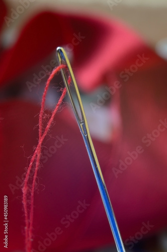 one sewing needles with red thread on a background of red fabric. close-up.