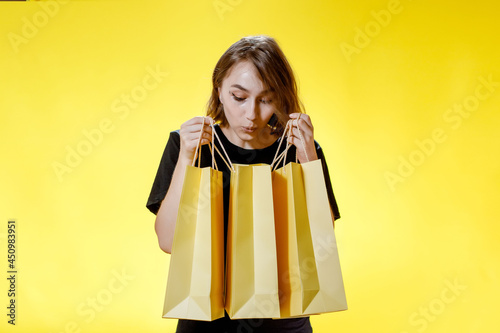 Joyful woman with packages on yellow background, shopping trip. Studio portrait. Black friday sale